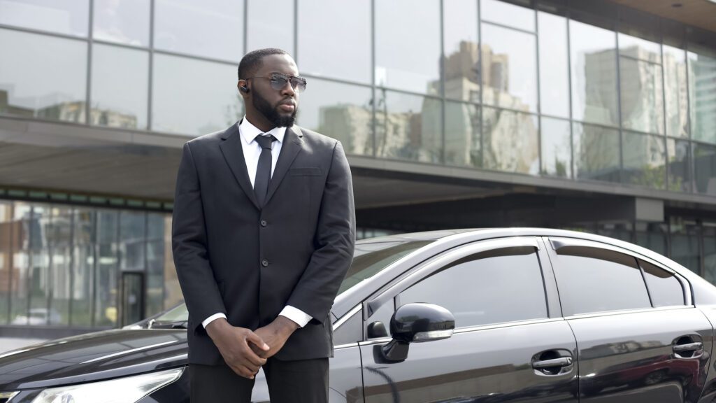Confident Afro-American driver standing by car, security guard service, business
